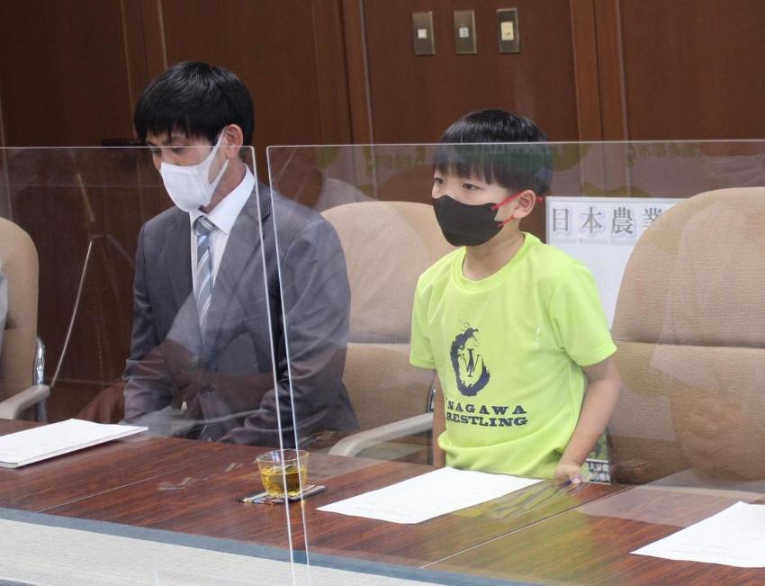 表敬訪問で、レスリングチームのTシャツを着た男の子が立ってお話している。