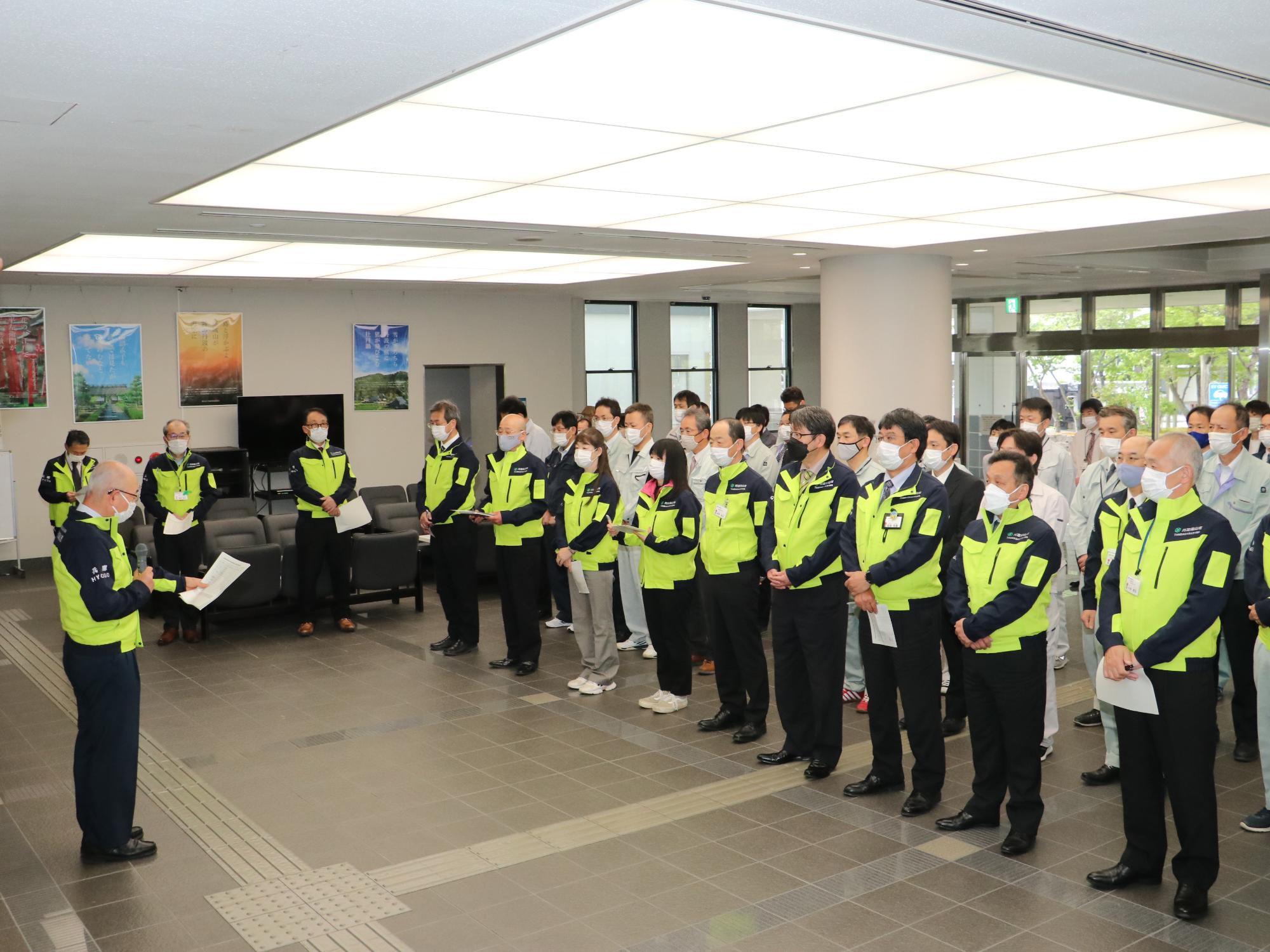 市民ホールで、防災服を着た市長が訓練で集まった幹部職員に訓示を行っている