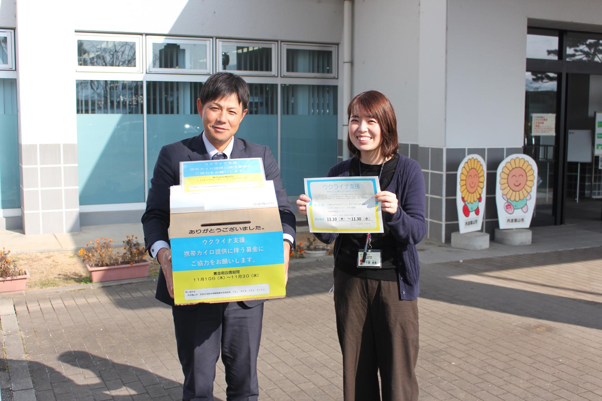 庁舎前で、男性職員がウクライナへの募金箱を手に持ち、その隣で女性職員がチラシを持っている