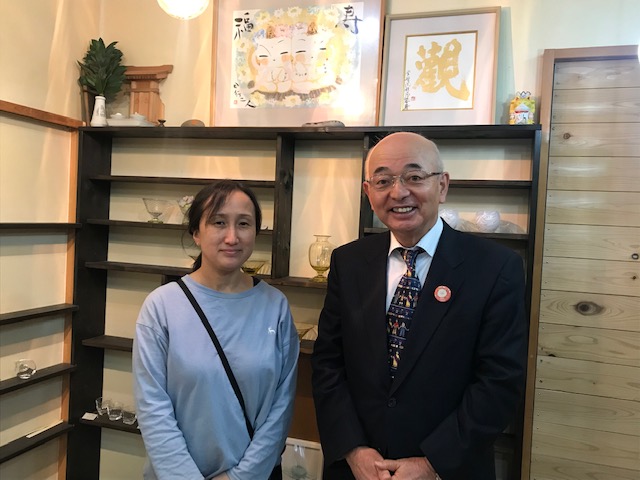 棚にガラスの食器が飾られている。市長と工房の方がその前で記念撮影。