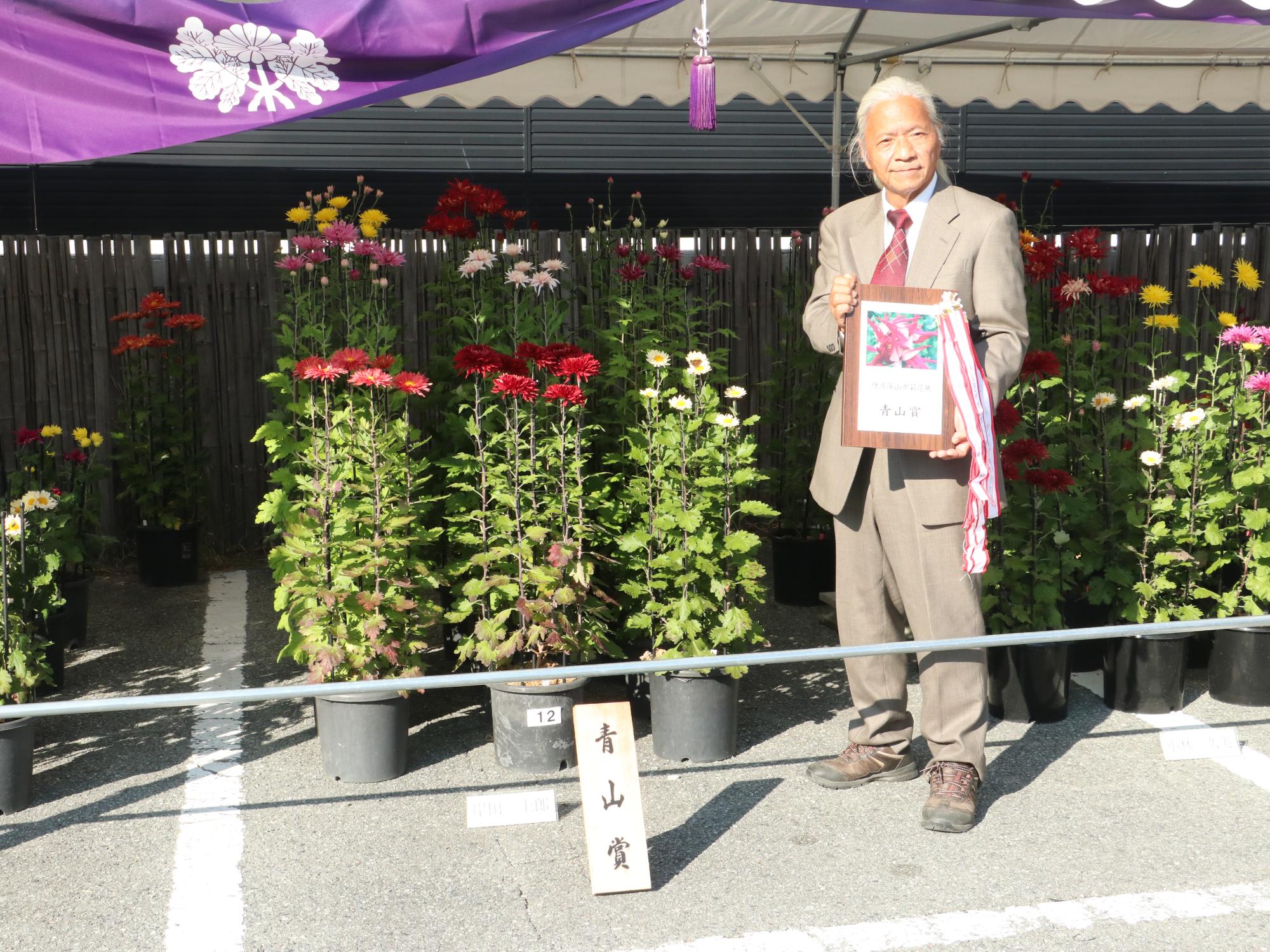 作品の前に青山賞のプレートを置き、受賞者が盾を持っている