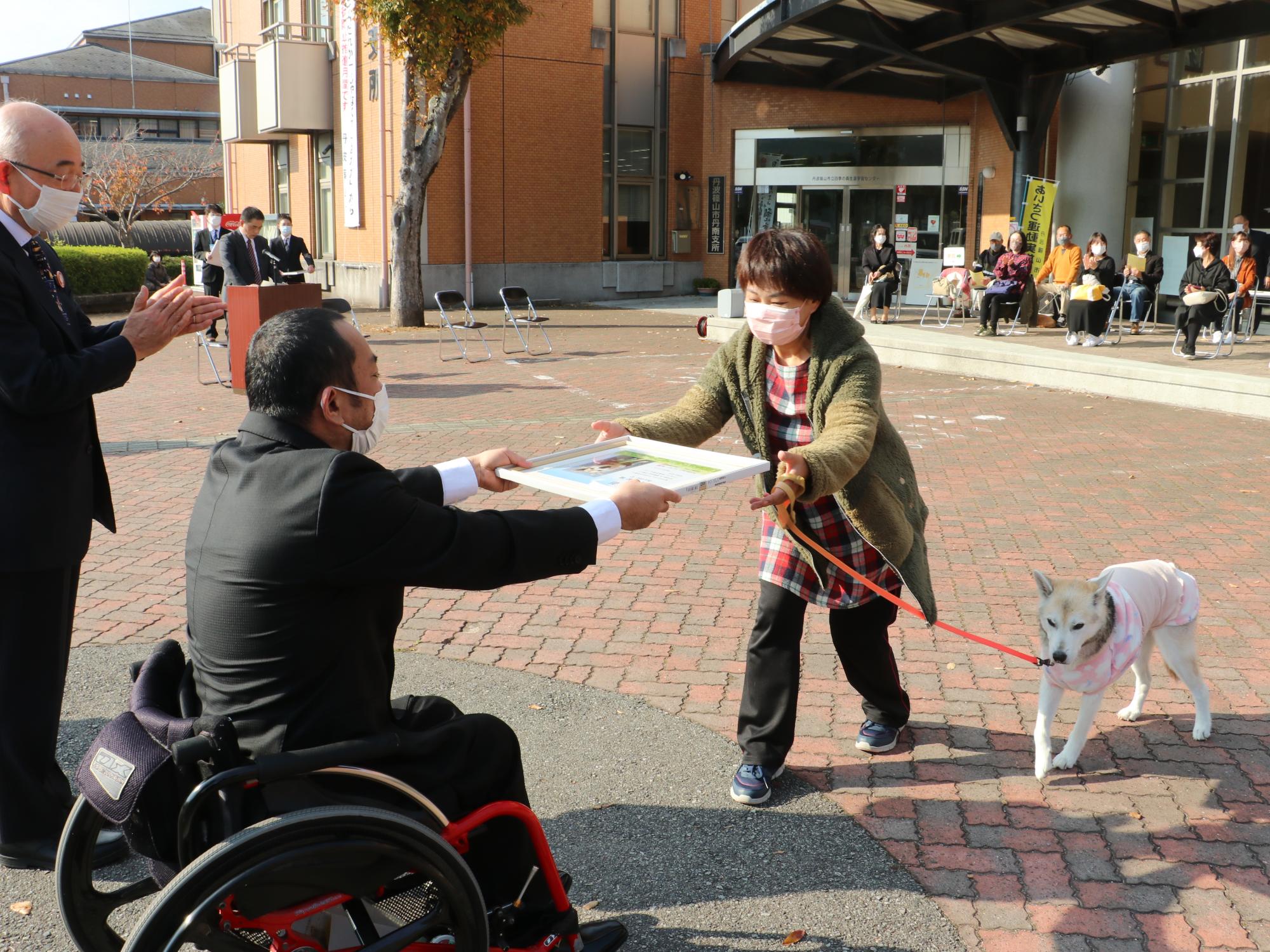 犬を連れた飼い主の方に表彰状を渡している