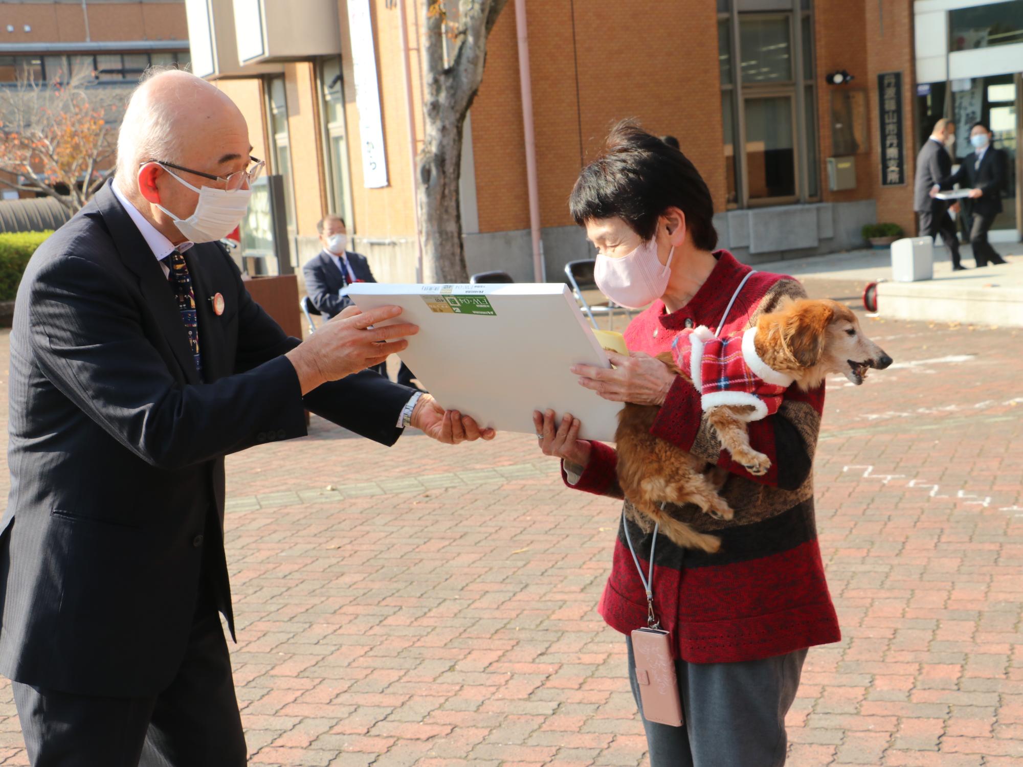 犬を抱っこした飼い主に表彰状を手渡している