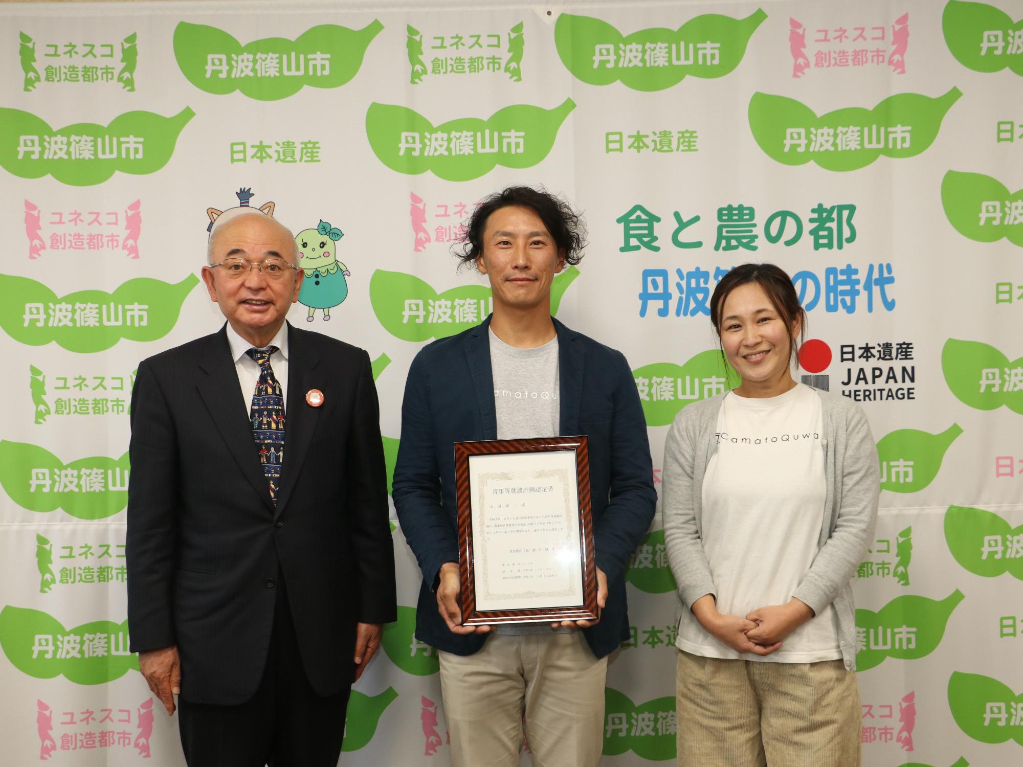 真ん中で男性が認定書を手に持っていて、その隣に女性、市長が並んで記念撮影
