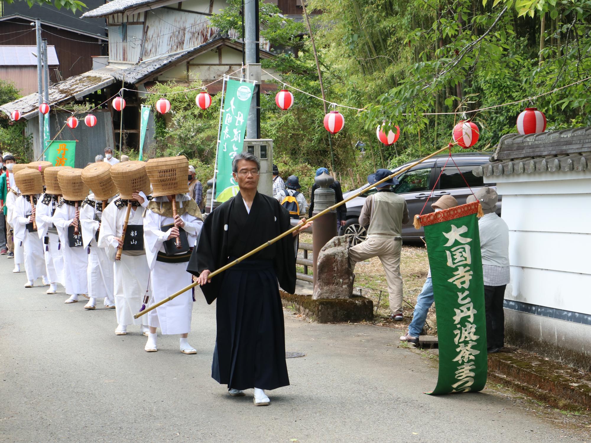 黒い着物を着て「大国寺と丹波茶まつり」というのぼりを持った男性を先頭に、傘をかぶって尺八を演奏されている方たちが練り歩いている