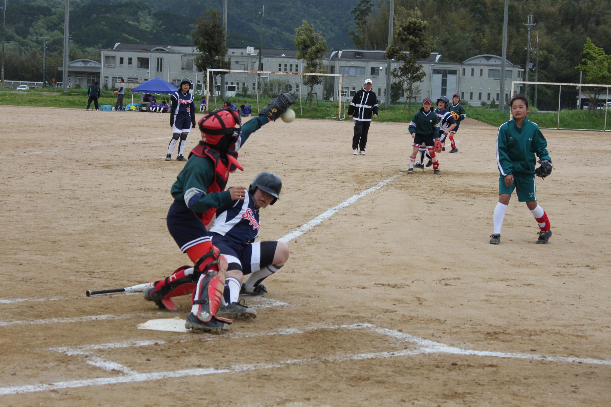 ソフトボールの試合で、ランナーがホームインし、キャッチャーがボールをキャッチしようとしている