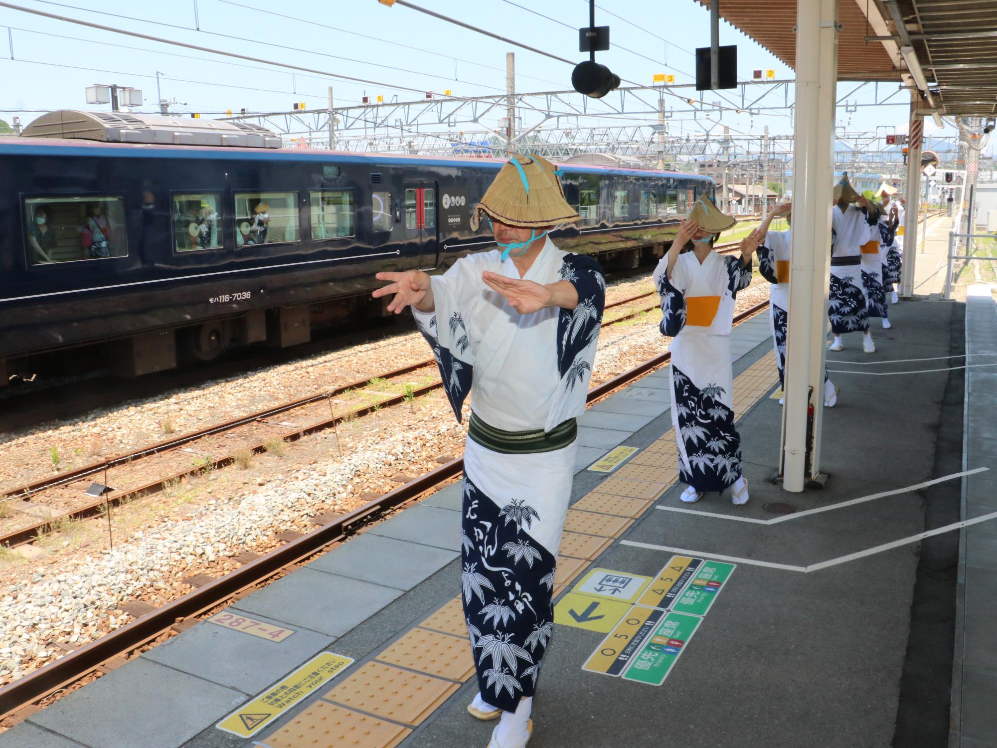 笹浴衣を着て編み笠をかぶった方数名が駅のホームでデカンショ踊りを披露している