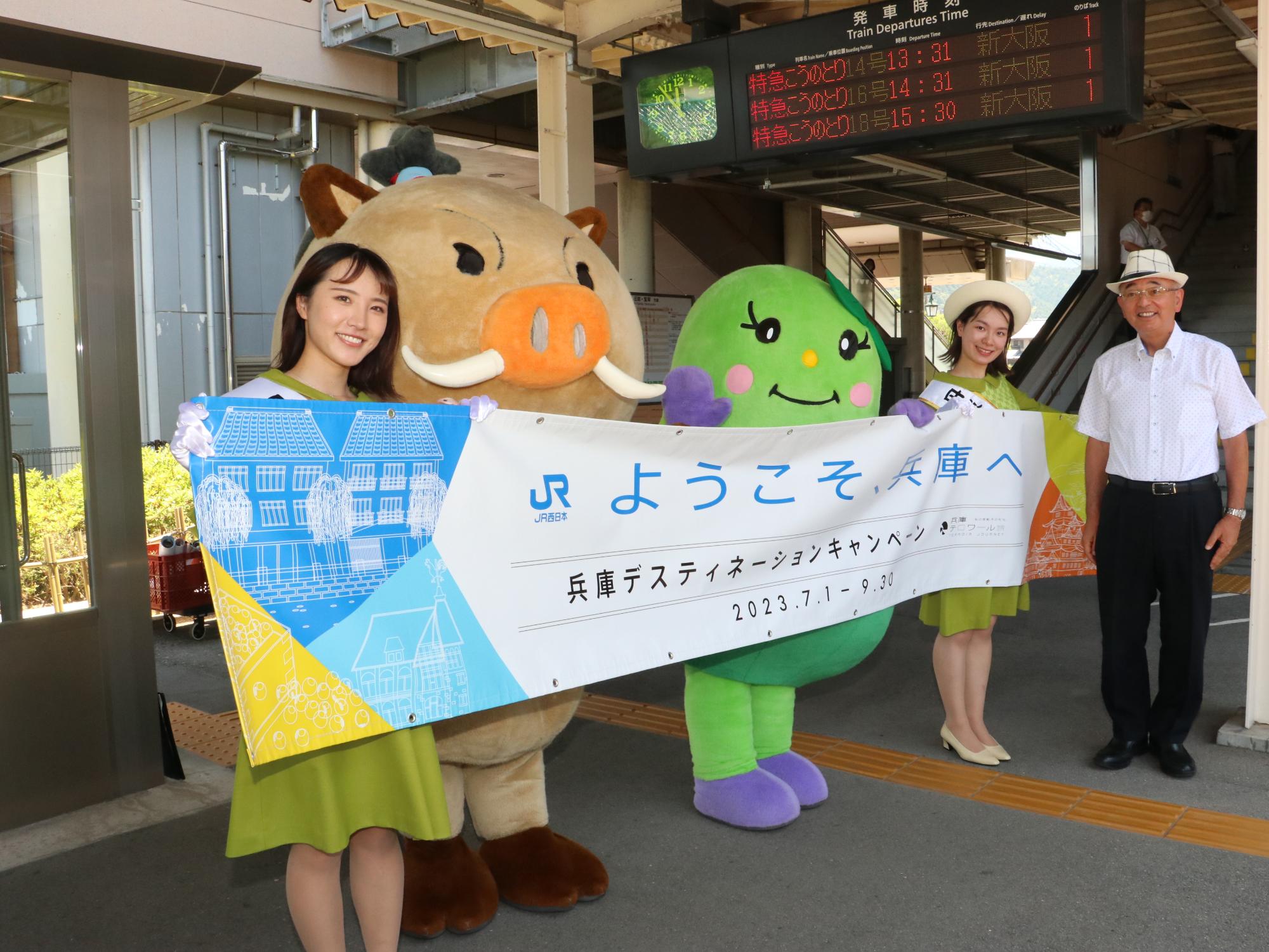 観光大使2人とまるいのまめりんが「ようこそ兵庫へ」とかかれた横断幕を持っている。その隣に市長が立っている