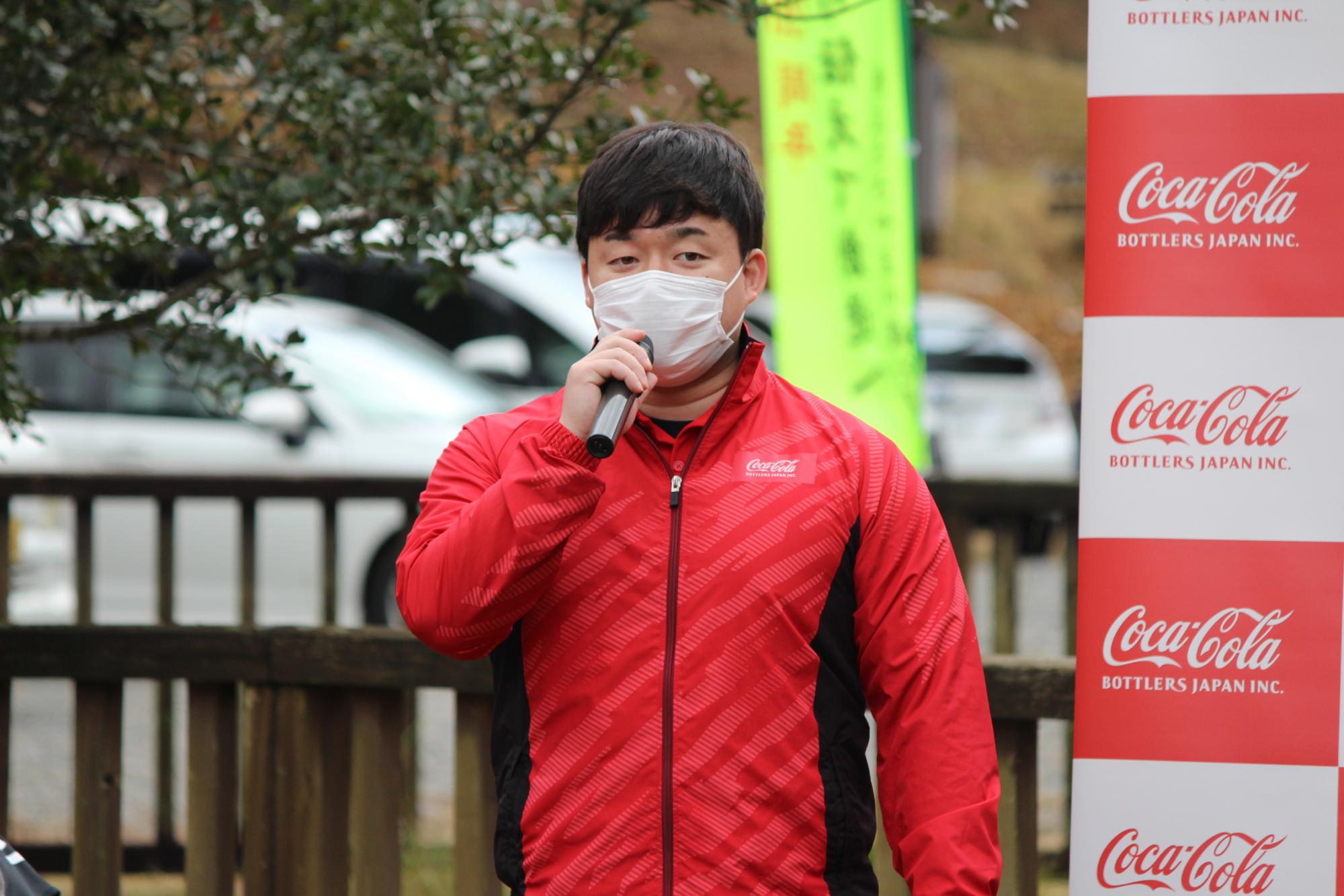 コカ・コーラの赤いジャケットを着た男性がマイクを持って話している