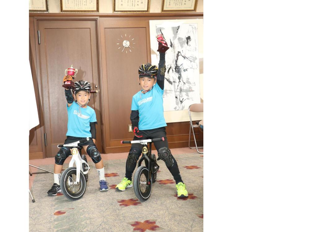 男の子二人がランバイクに乗っていて、それぞれカップを持った手をあげている