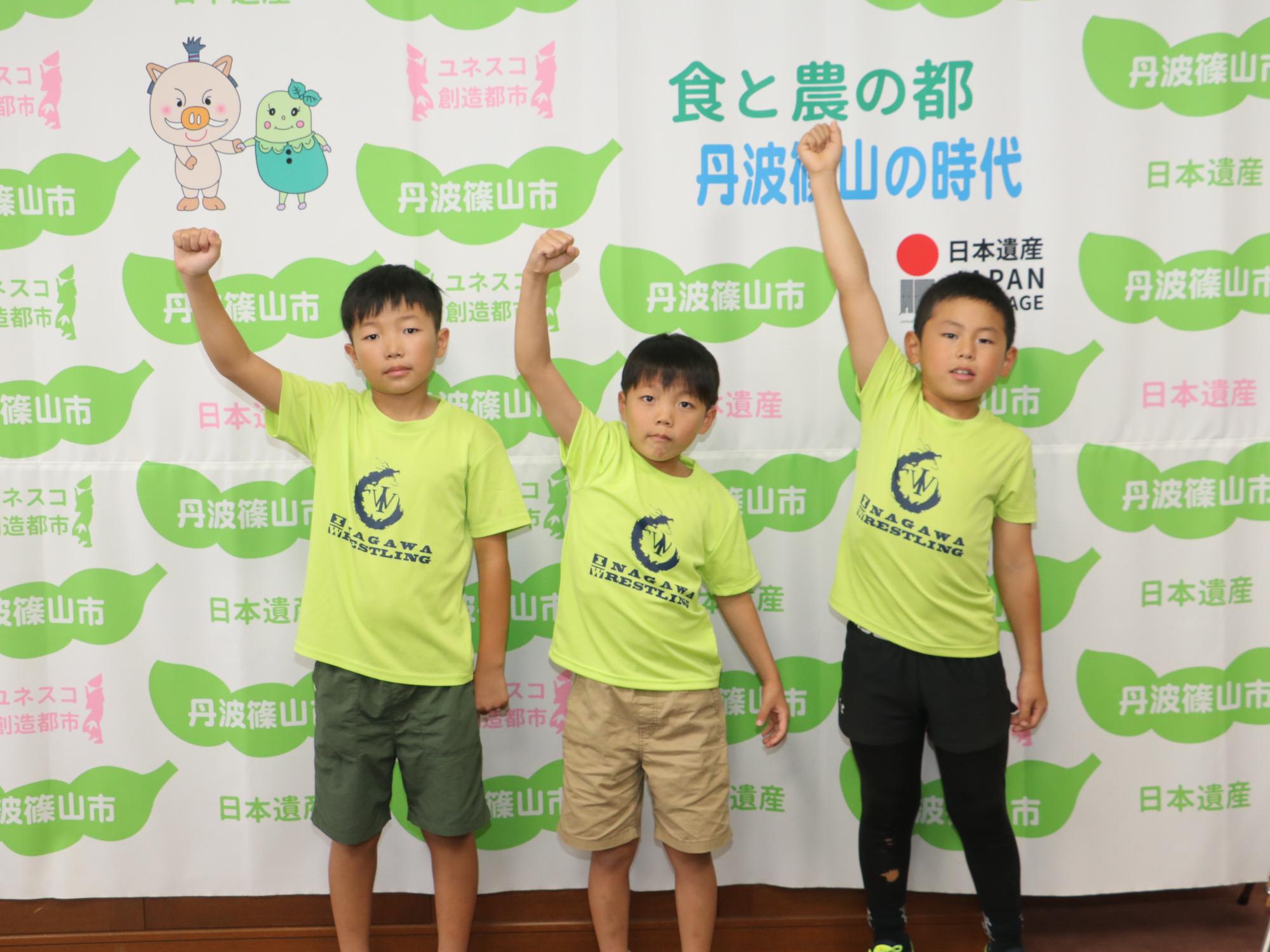 同じ黄緑色のTシャツを着た男の子3人が片手をあげている