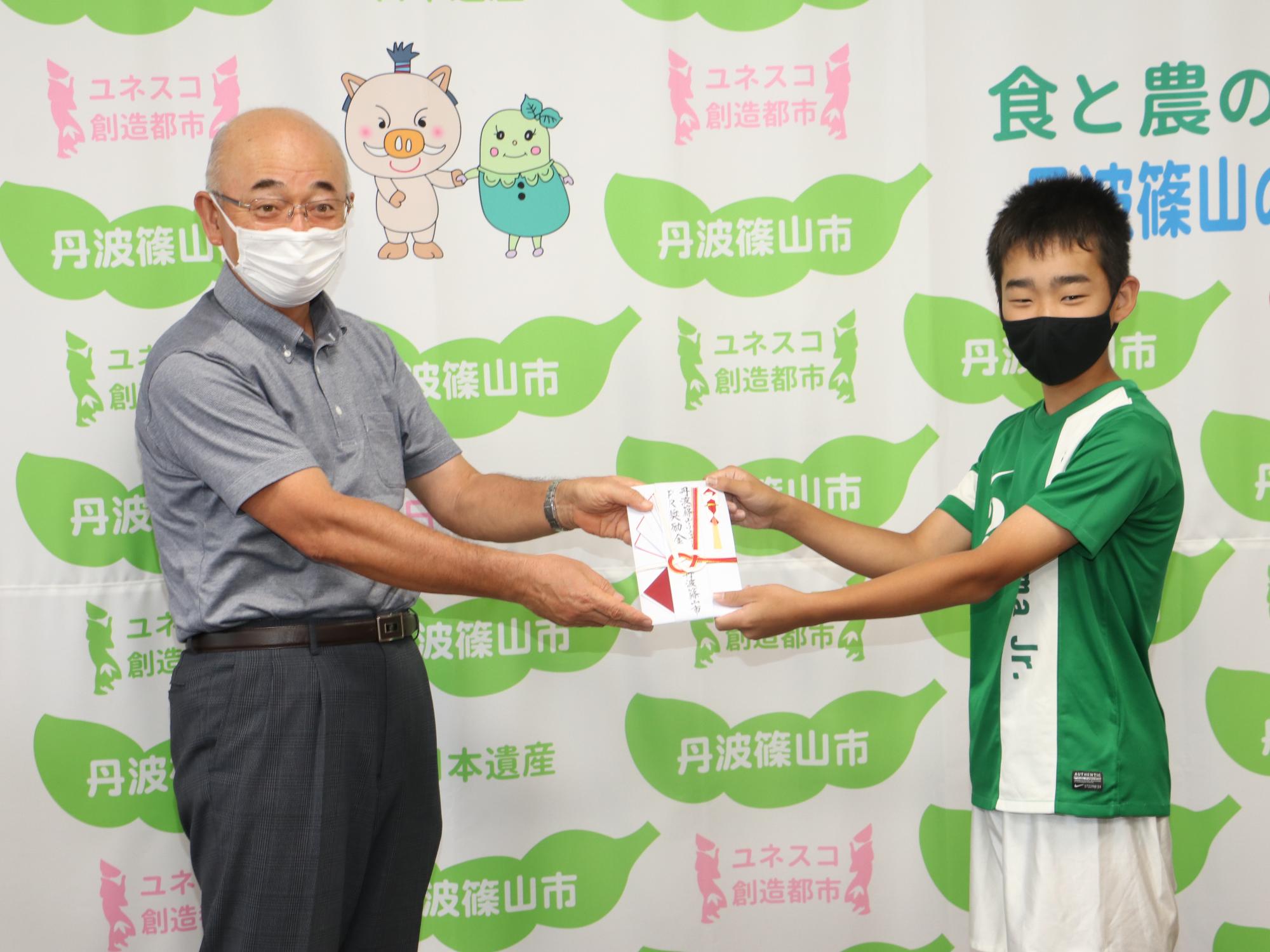 ホッケーのユニフォームを着た男の子が、市長から奨励金の目録を手渡されている