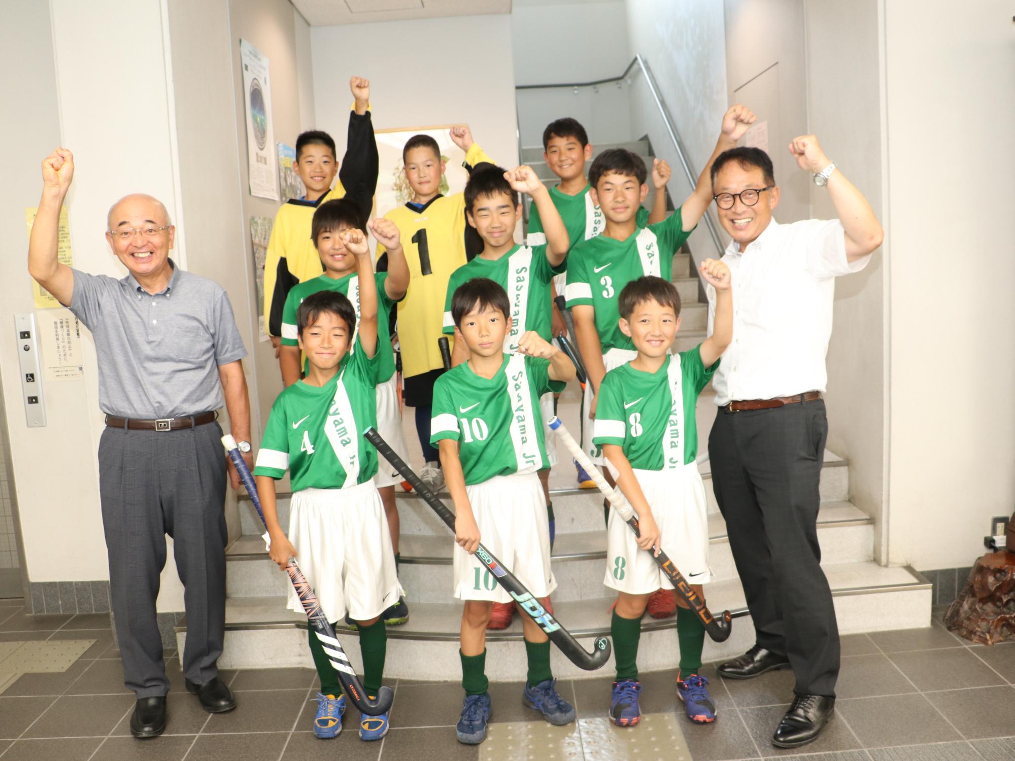 市長、教育長、ホッケーチームのユニフォームを着た子ども達の記念撮影