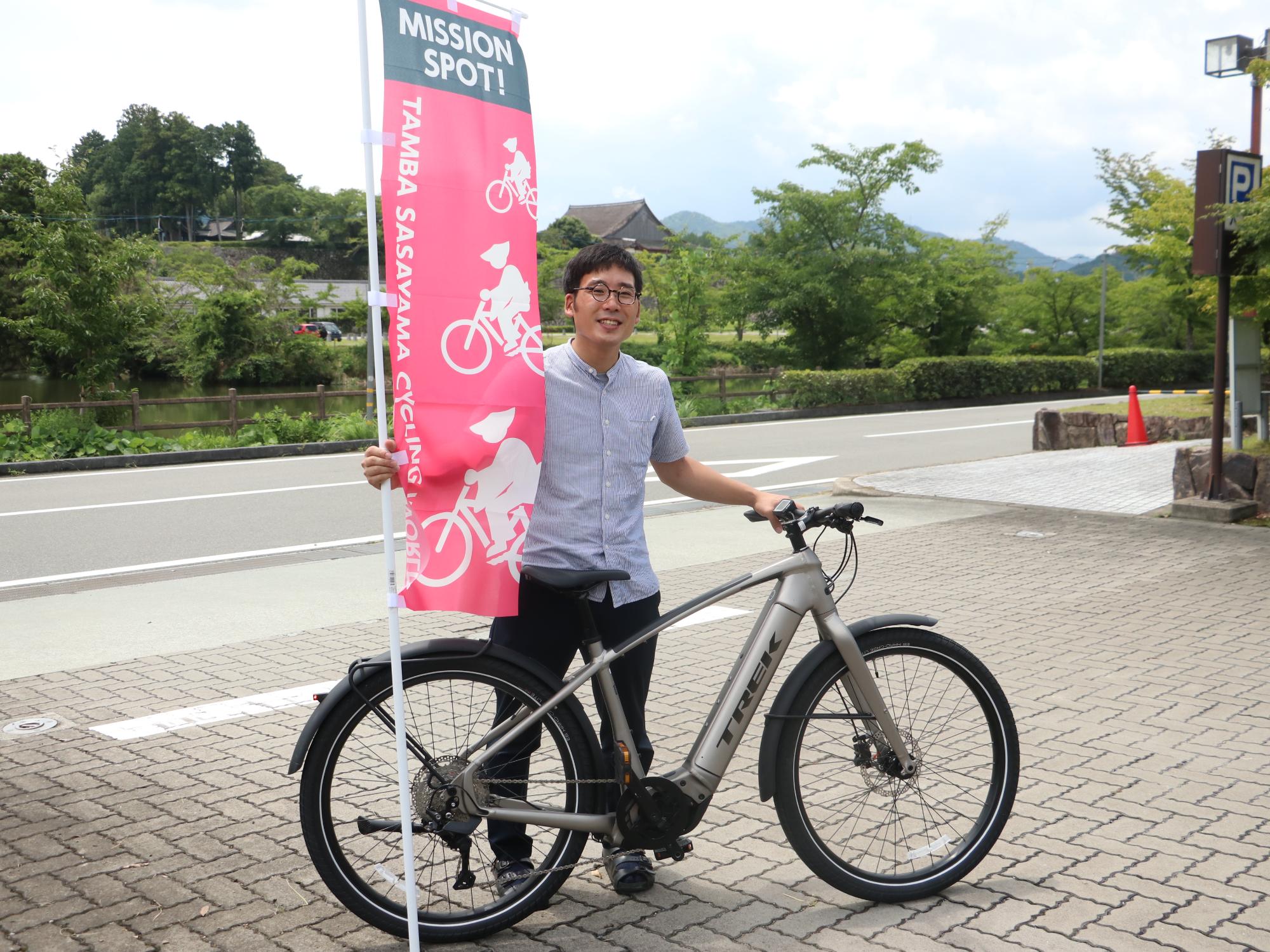 自転車を立てかけ、サイクリングワールドののぼり旗を持っている男性