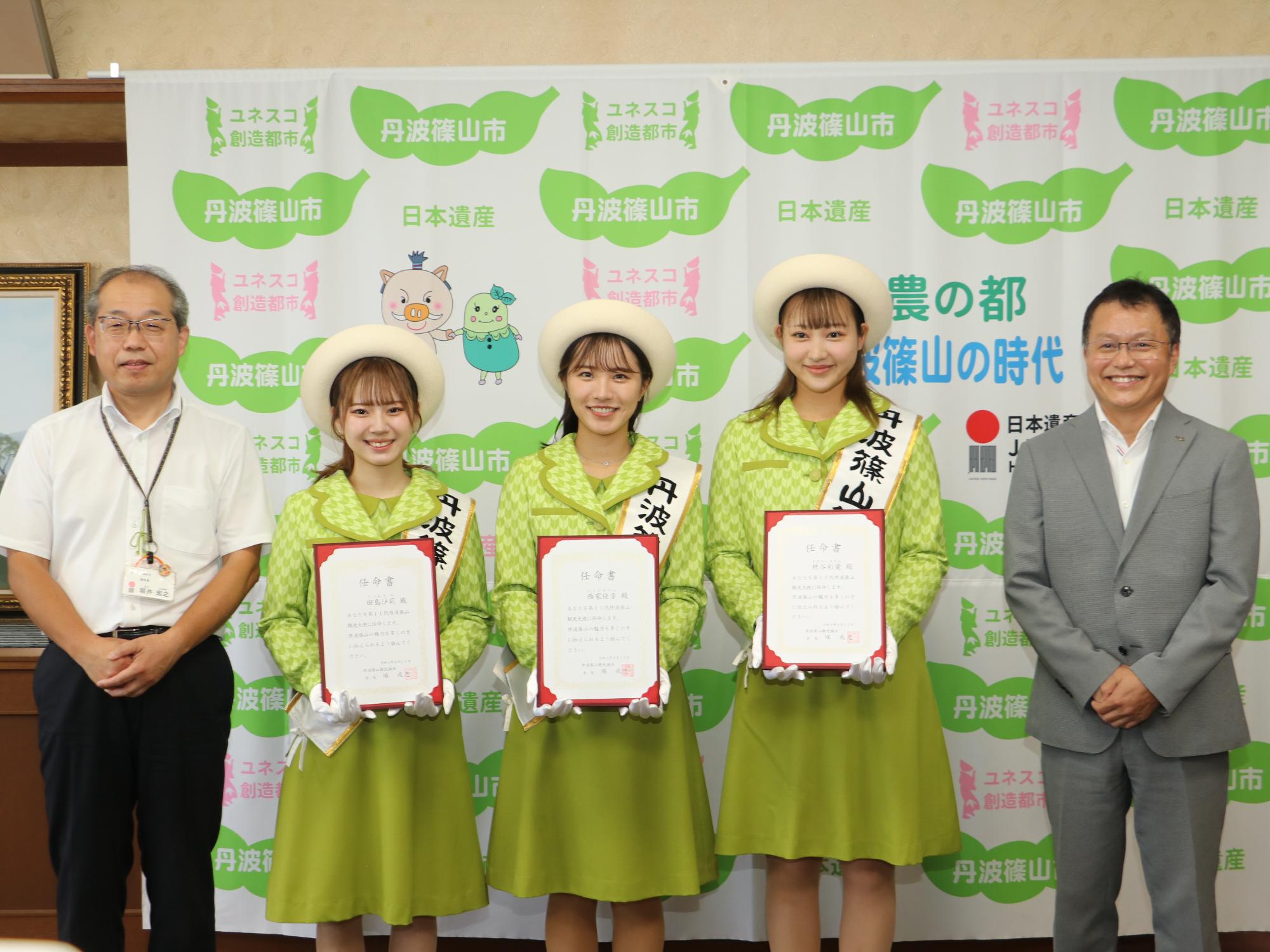 3人の観光大使が任命書を手に持っていて、両隣に副市長、観光協会会長が並んでいる