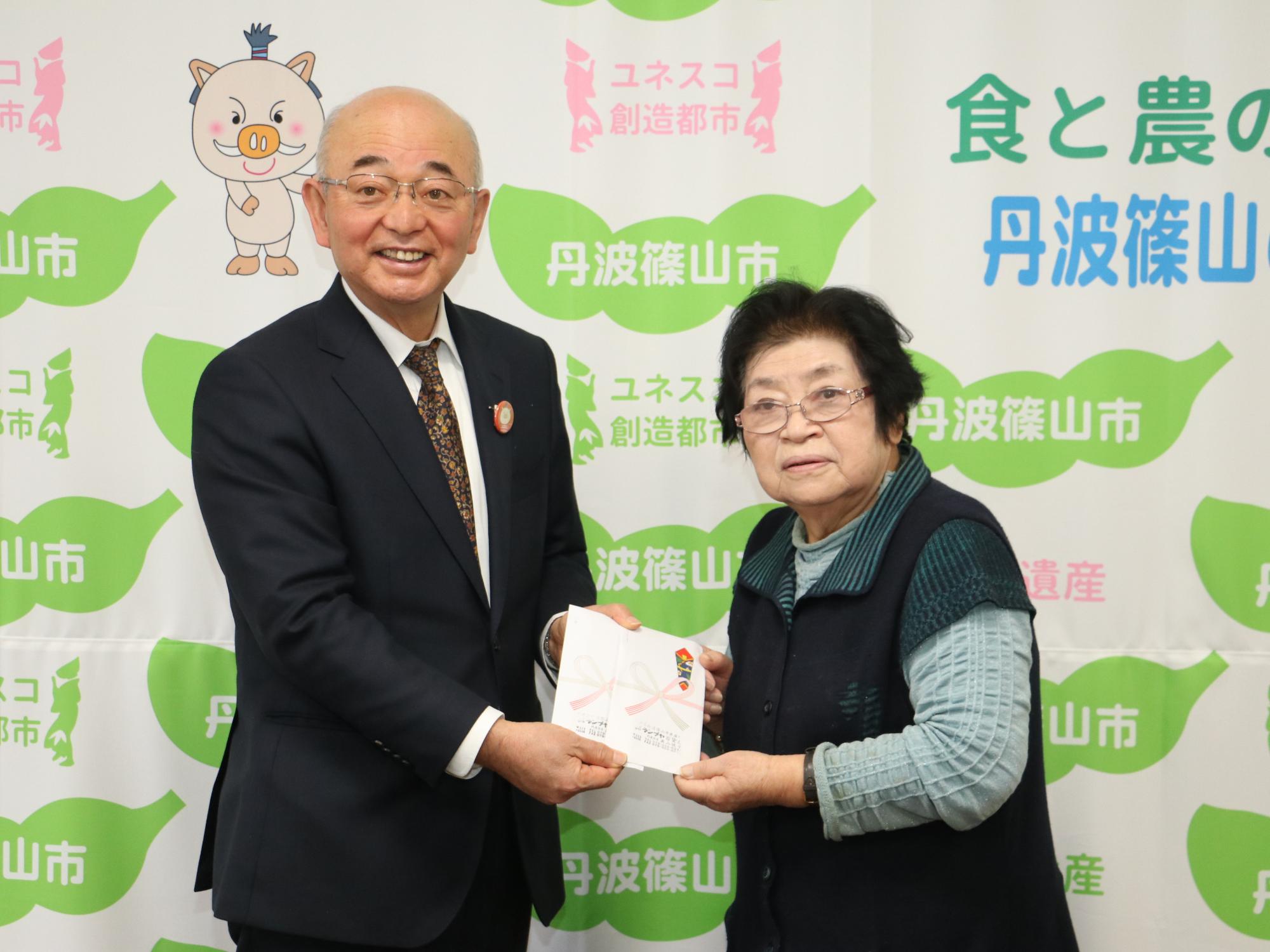 女性が義援金を市長に手渡されている