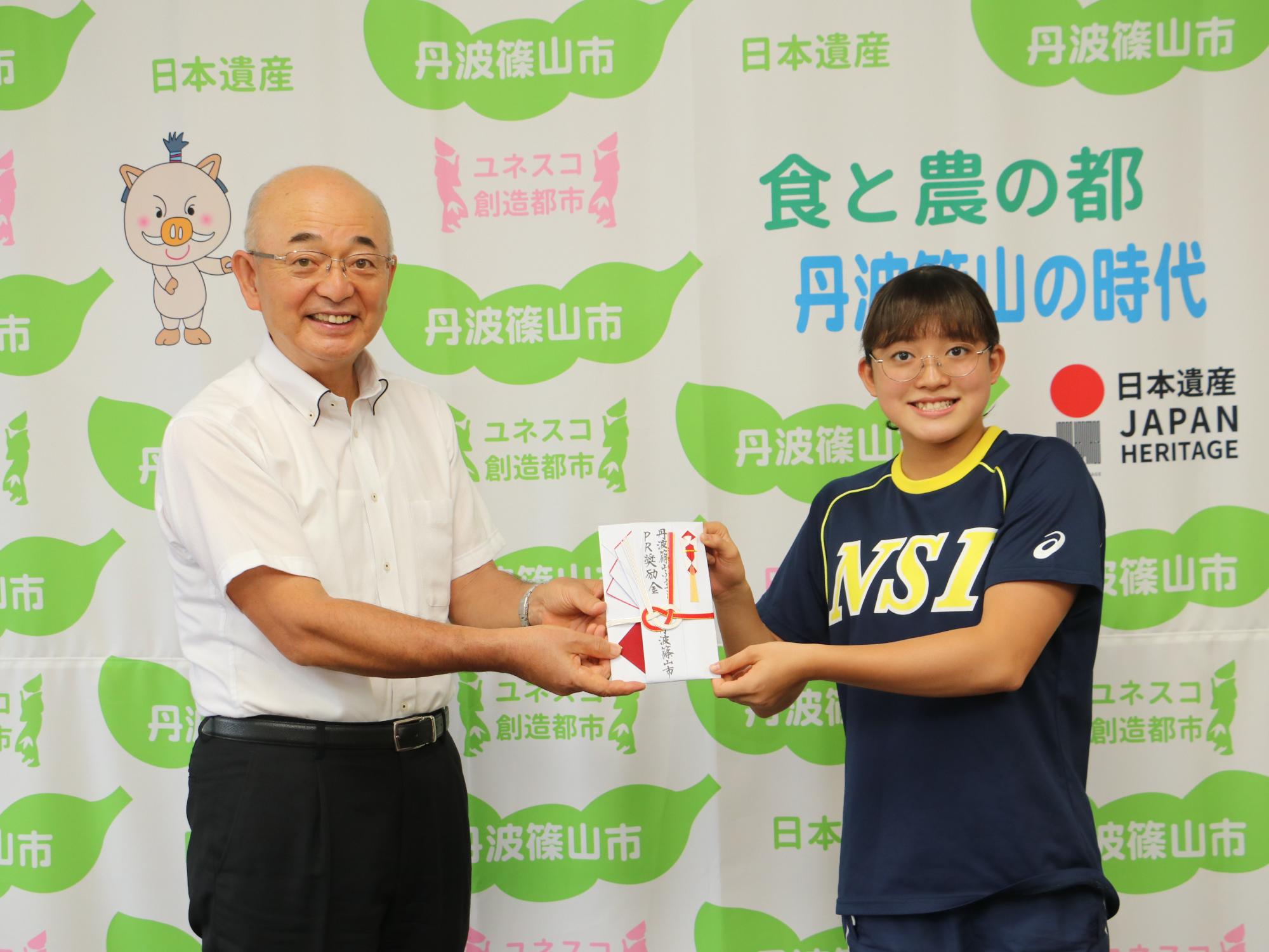 市長が奨励金の目録を水泳クラブのユニフォームを着た女の子に渡している