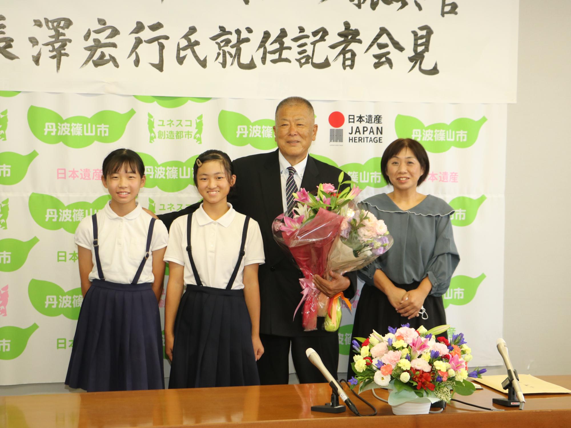 花束を持っている長沢先生と地元ソフトボールチームの女の子2人と、産業高校OBの女性