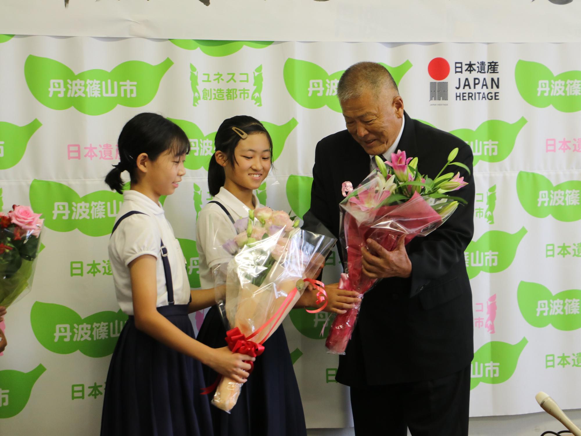 制服を着た女の子2人から、長沢先生が花束を受け取っている