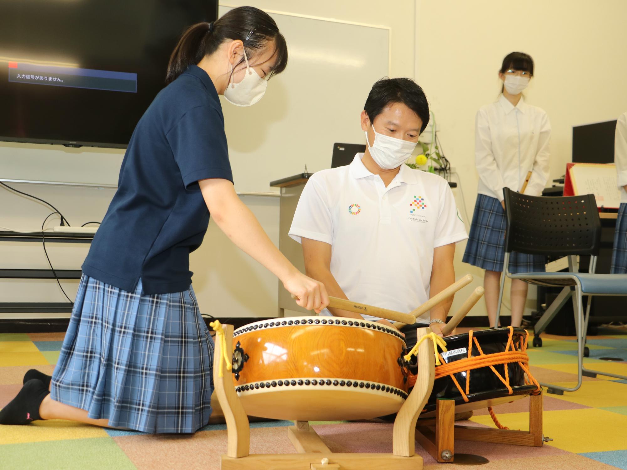 女子生徒が、知事に太鼓のたたき方を教えている