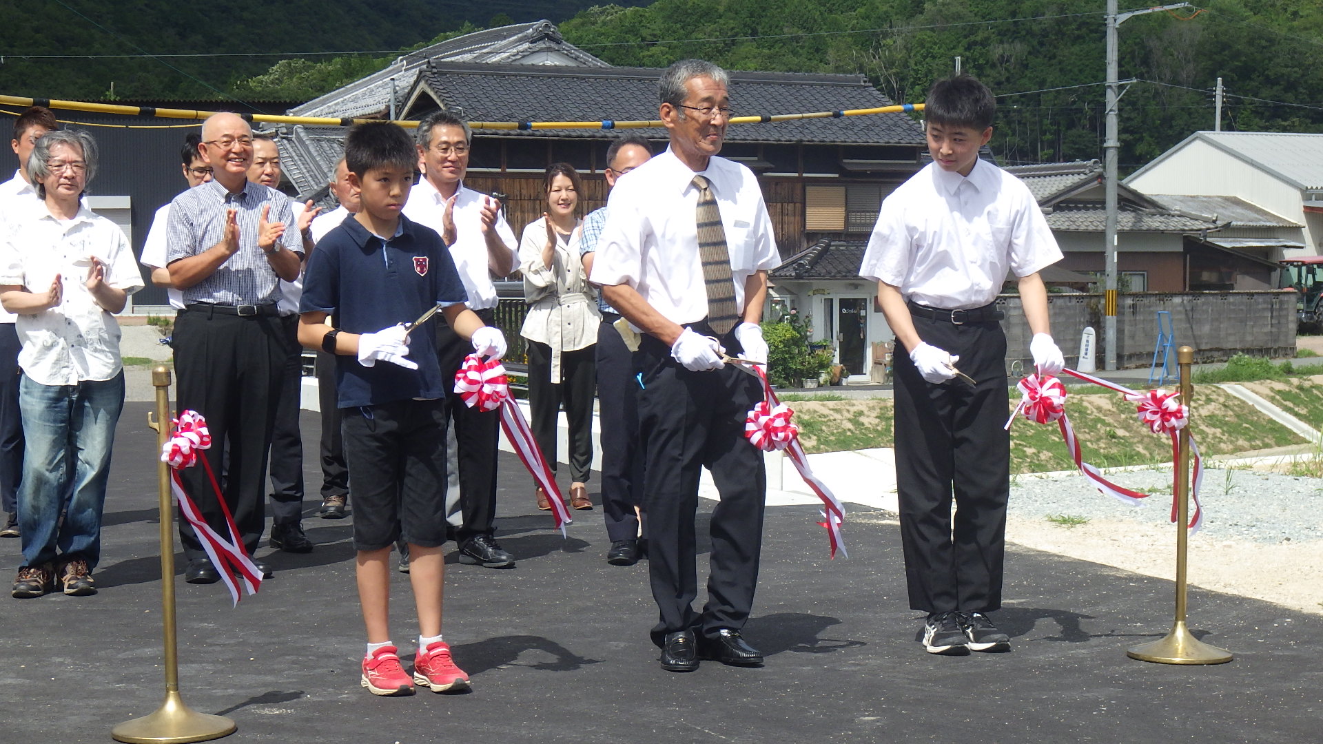 橋の渡り初め式で、地元のこどもと役員の方がテープカットを行った。後ろで関係者が拍手している