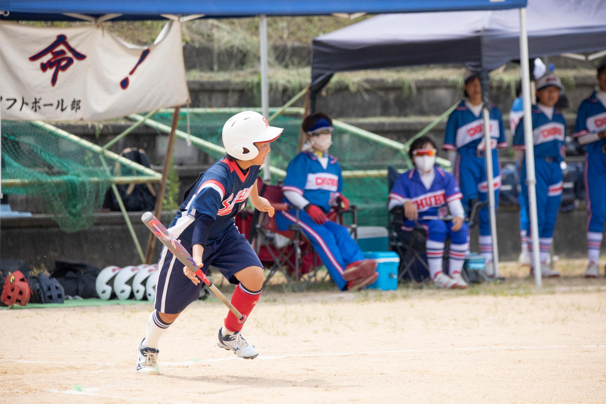 ユニフォームを着た女の子がバットを振って走っている