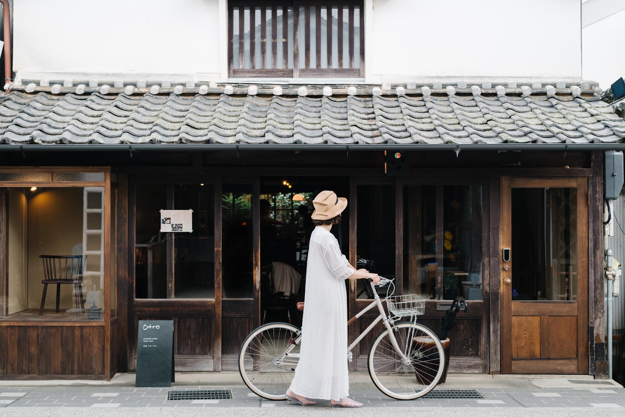 古民家でお店をされている前を、女性が自転車を押しながら歩いている
