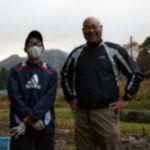 作業着姿の経営者構井さんと研修生の高橋さんが畑内で笑顔の写真