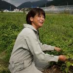 代表の湊さんが作業着姿で自身が育てた野菜の前に座って笑顔で話しをしている写真