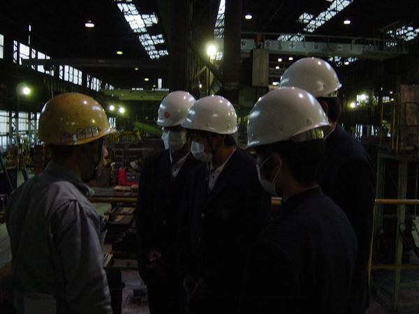 ヘルメットとマスクを装着し、工場見学をする学生たちの写真
