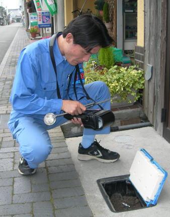 青い作業服を着た検針員が水道メーターの確認をしている写真