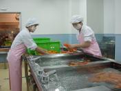 白衣にピンクのエプロンをした給食センターの職員2名が、大きな水槽で、にんじんを洗っている写真