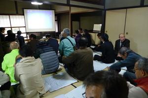 大型スクリーンが用意された和室で講演会に正座して参加している人々の写真（篠山地区：鳳凰会館）