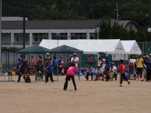 運動場で子供たち男女混合チームがソフトボールをしている様子の写真