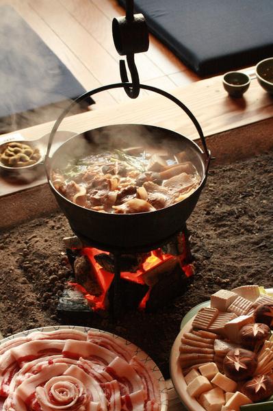 囲炉裏の中で炭火にかけられ、ぐつぐつとおいしそうに煮立っているぼたん鍋の写真