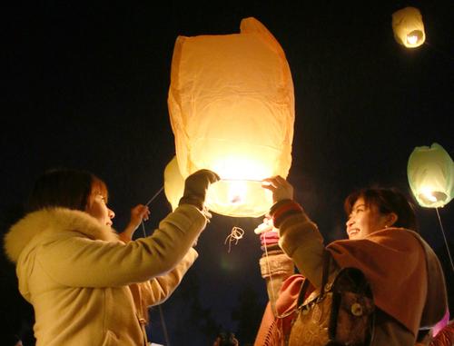 夜空に飛ぶ3つのランタンとオレンジ色のフライングランタンに触れる二人の若い女性の写真