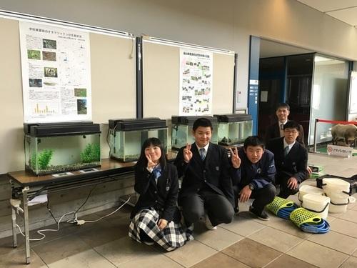 水槽が4つ並べられた机の前でピースサインをして笑顔で写真に写る篠山東雲高校自然科学部のみなさんの写真
