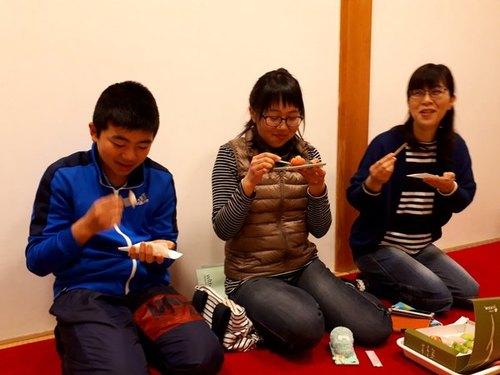 3名が正座して和菓子を試食し微笑んでいる写真