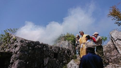 多紀連山頂上にて、御嶽と弥十郎ヶ嶽の間で白い煙があがるのろしと旗による交信を行う様子の写真