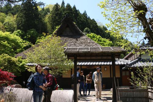 新緑の中にたたずむ昔ながらの瓦葺きの屋根の籠坊温泉の建物と見学する参加者の方々の写真
