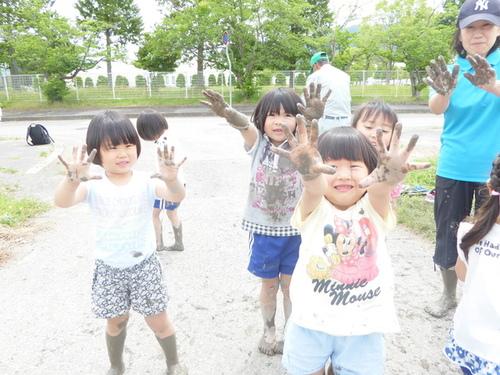 数名の子供が泥んこになった手をカメラに向けて見せている写真
