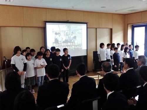 フォーラム参加者の前で、大きなプロジェクタースクリーンの左右に並んだ篠山小学校4年大組の皆さんの写真