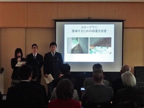 「スロープ下に誘導するための段差を設置」と書かれた資料をプロジェクターに映しながら説明する篠山東雲高校自然科学部の皆さんの写真