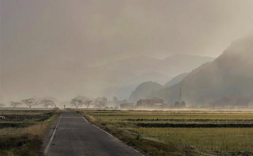 真っ直ぐな道の先にある霧に包まれた集落と山々の見事な写真