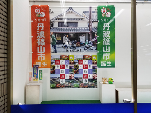 広報ショーウインドーの中に飾られた「5月1日丹波篠山市誕生」と書かれたポスターとのぼり旗の写真