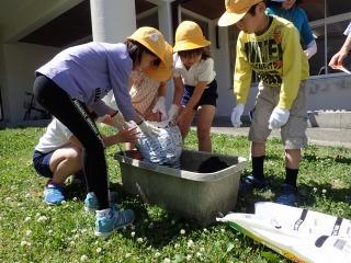 軍手をした子供たちが長方形の植木鉢に土を敷いてる様子の写真