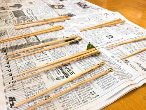 新聞紙の上に並べられた様々な模様の入った7膳のお箸の写真