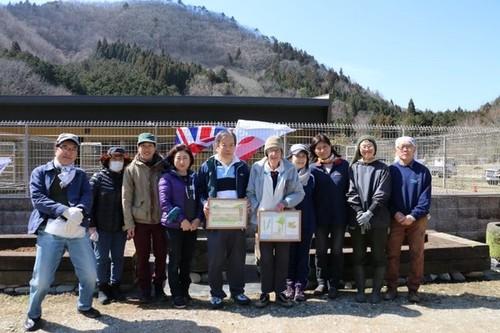 日本とイギリスの国旗を背景に、笑顔で写真に写るオリバーさんと関西日英協会の皆さんの写真