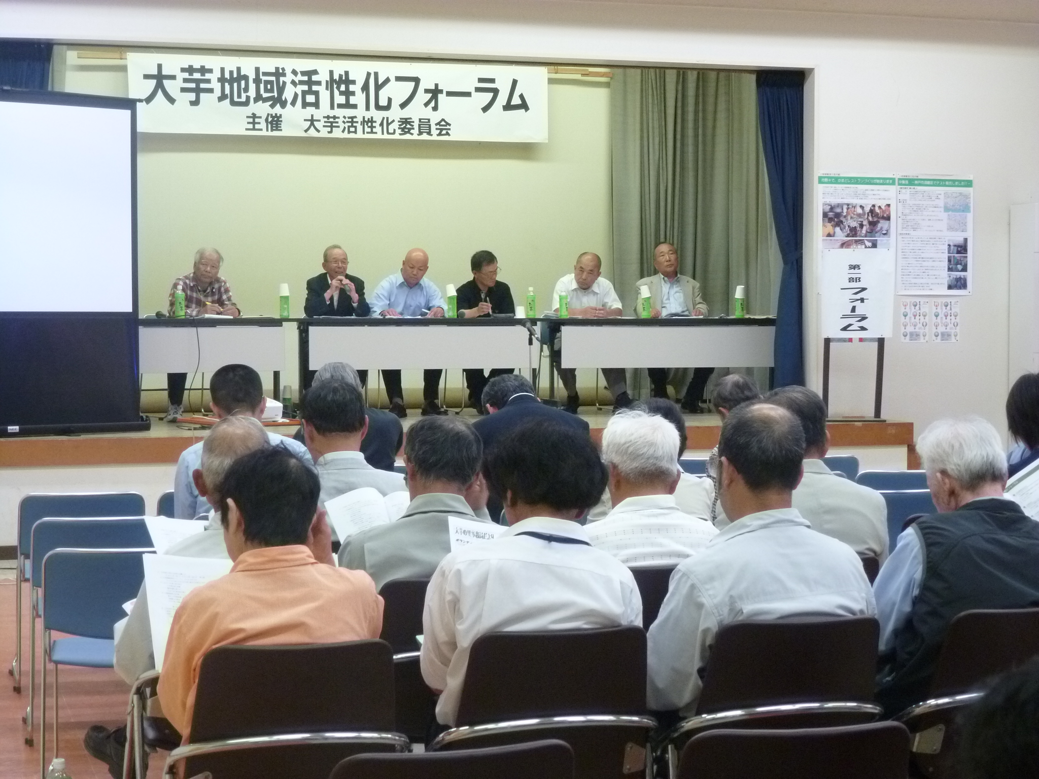 大芋地域活性化フォーラムにて、ステージ上に設置された椅子に座って話をする大芋活性化委員会の皆さんと向かいあって座る参加者の皆さんの写真