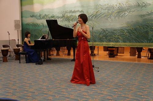 赤いドレスを着てマイクを持ち歌を歌っている女性出演者の写真